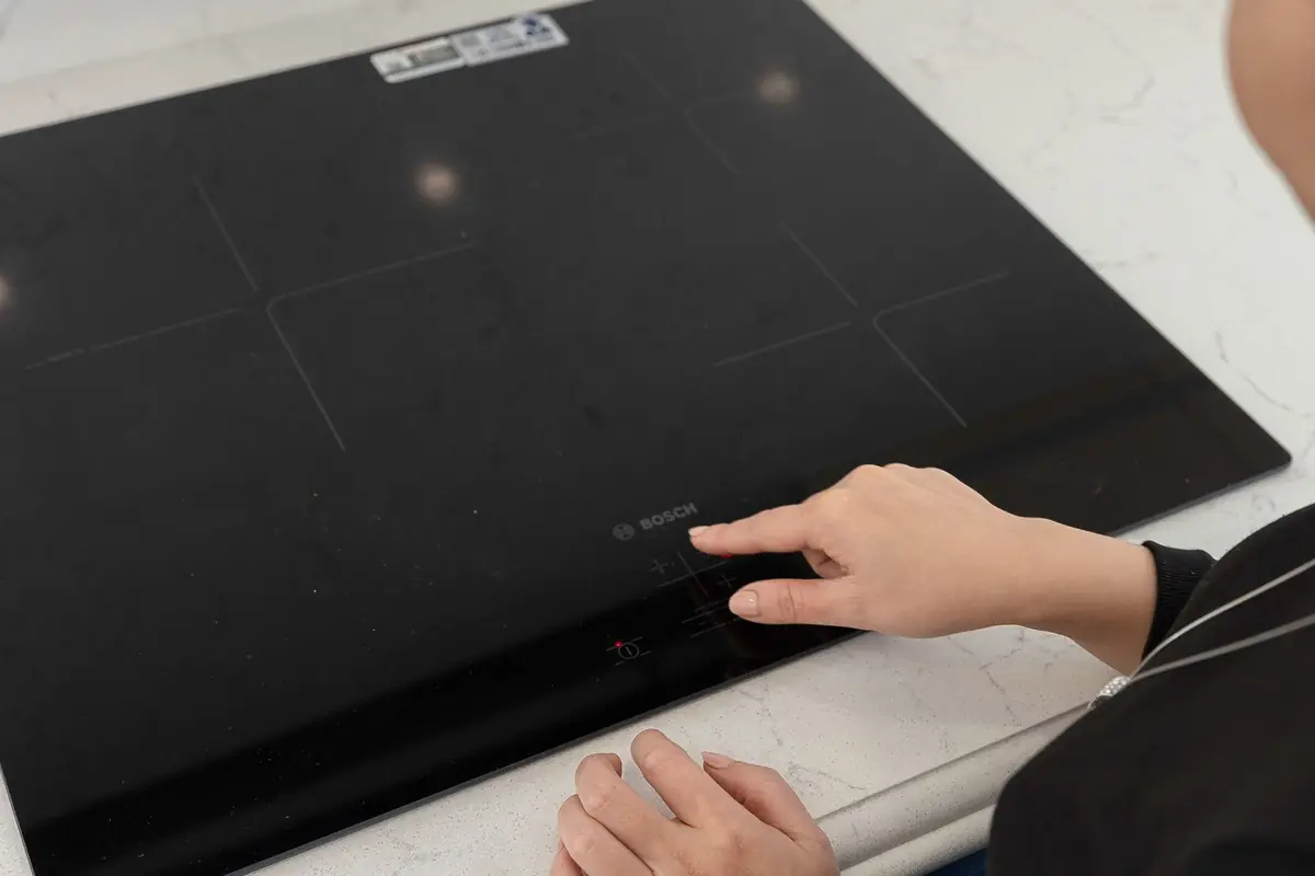 A hand pressing the touch controls on a black induction cooktop