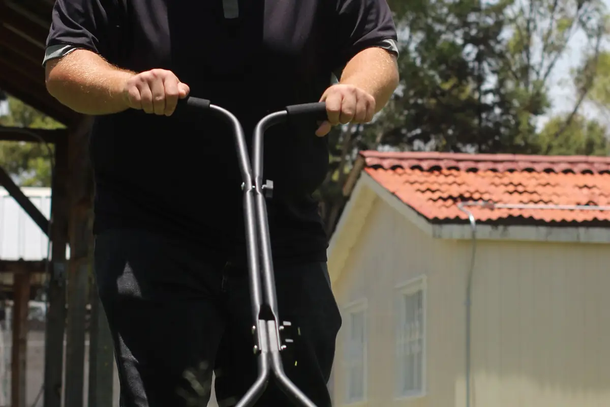 A person pushing a manual reel mower on a sunny lawn