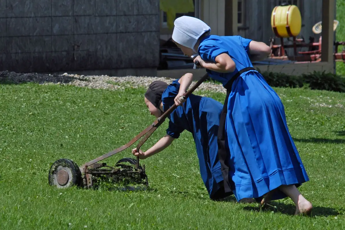 Two women pushing manual reel mowers across a lawn