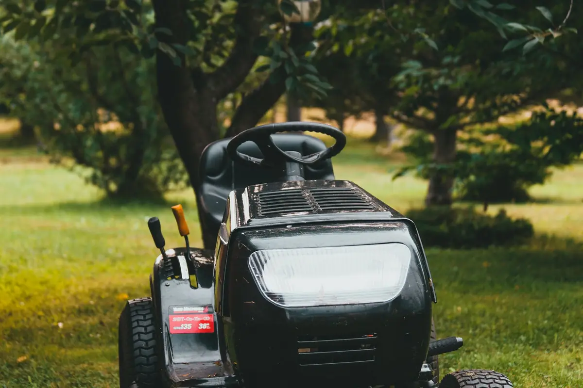 A black riding lawn mower parked on a tree-lined backyard lawn