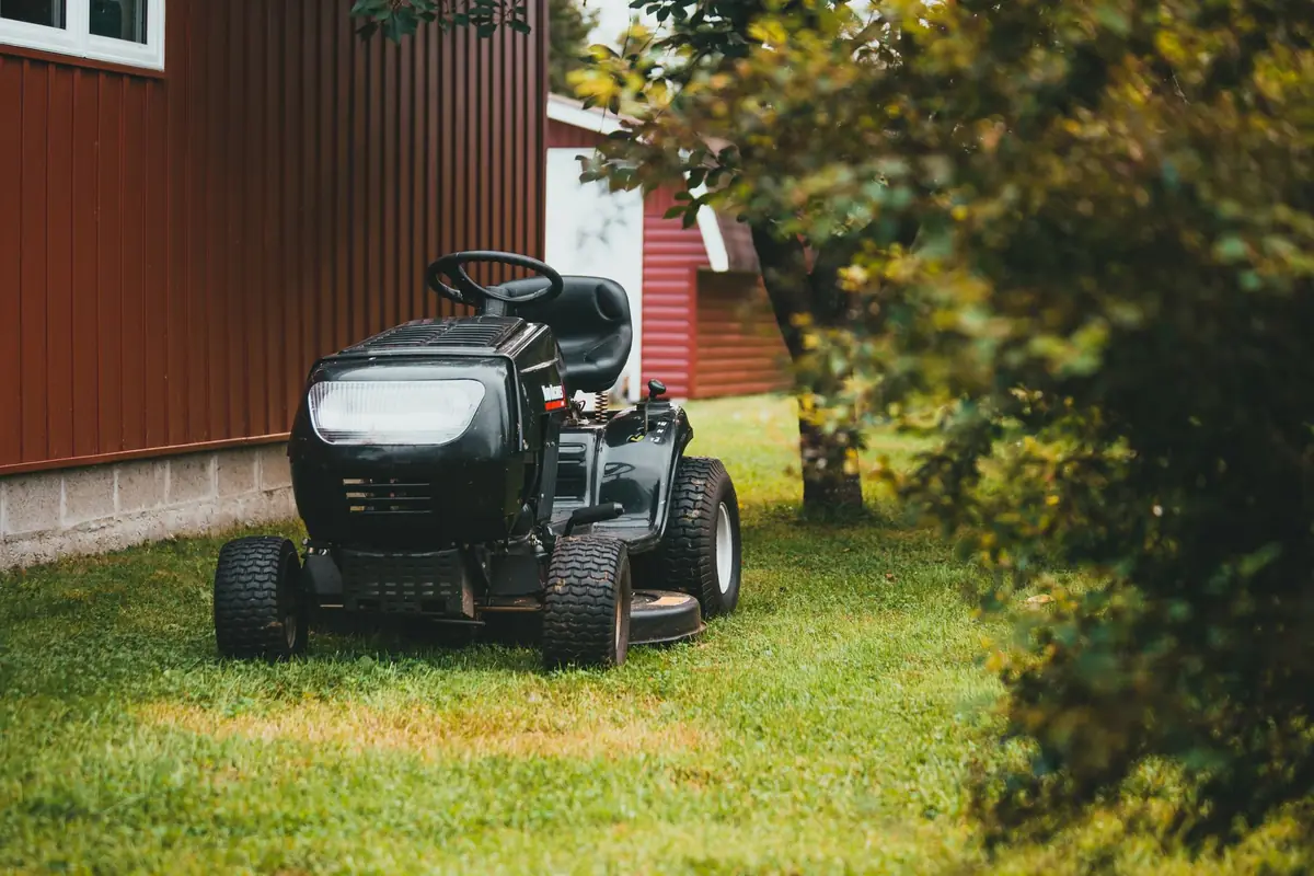 A black ride-on mower on the grass beside a red barn