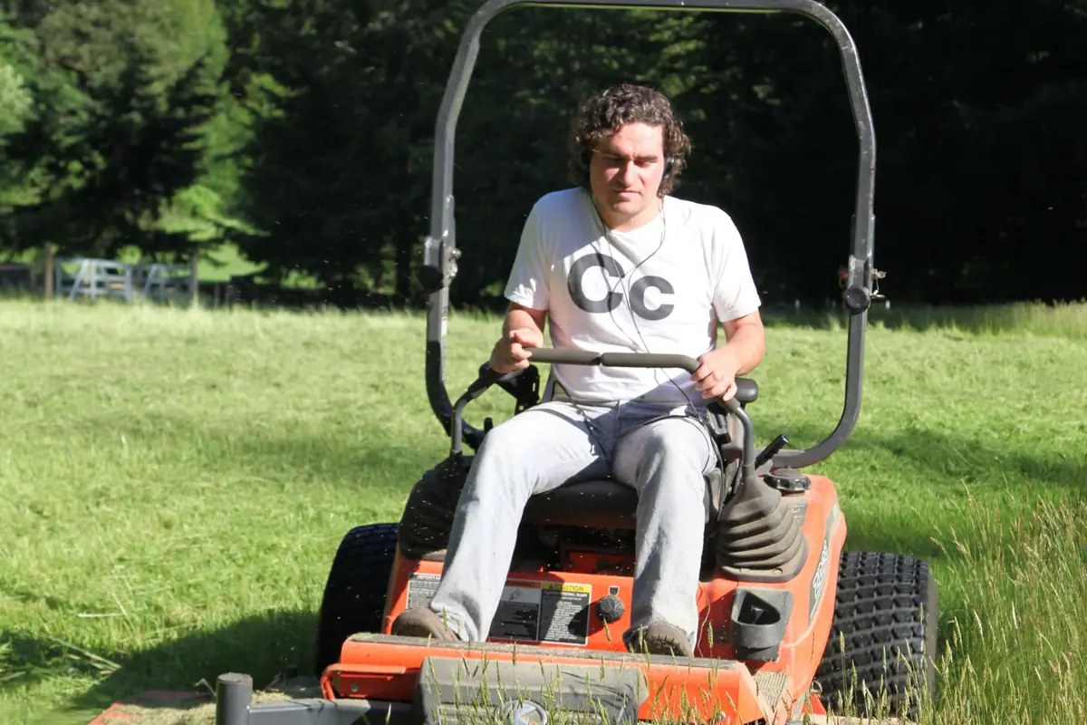 A man driving an orange zero-turn mower across a green lawn