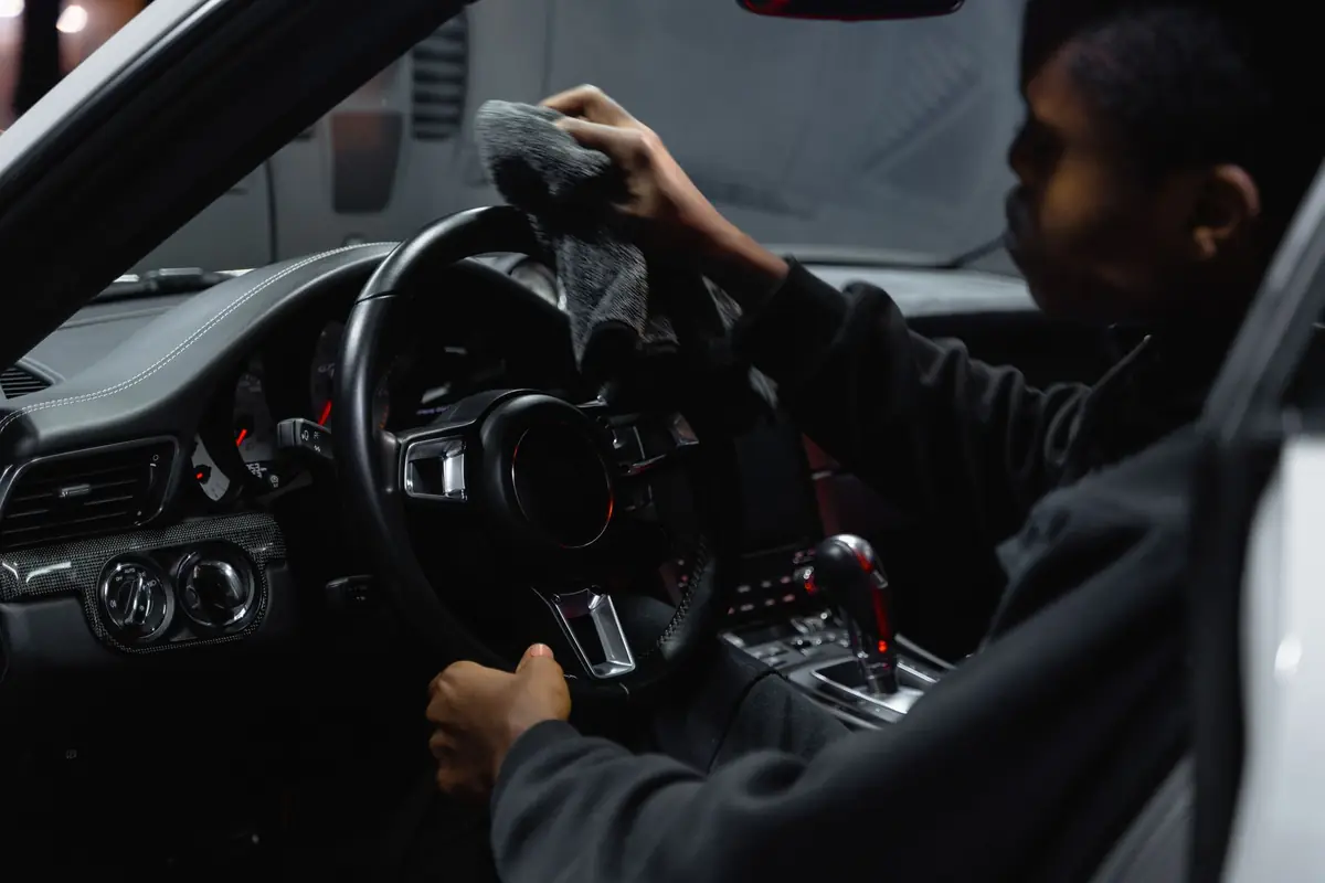 A person wiping down a car steering wheel with a cloth