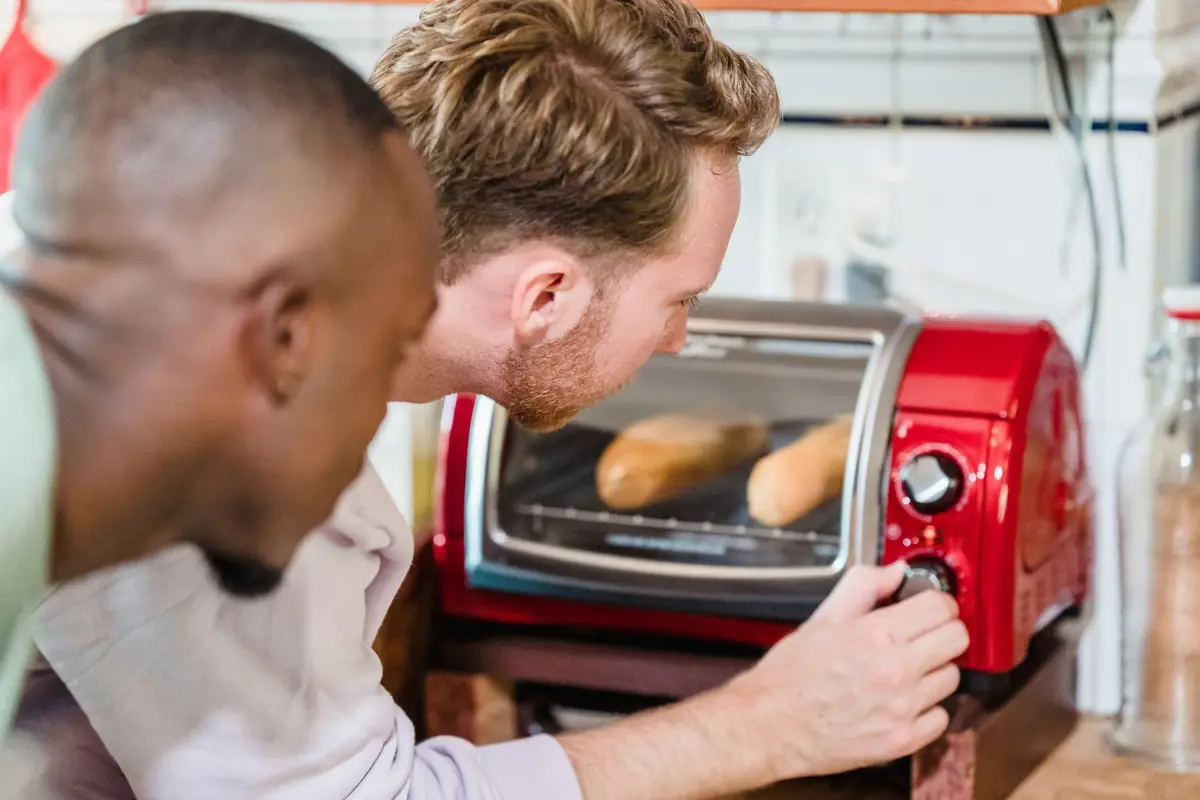 Two people watching bread toast in a red toaster oven