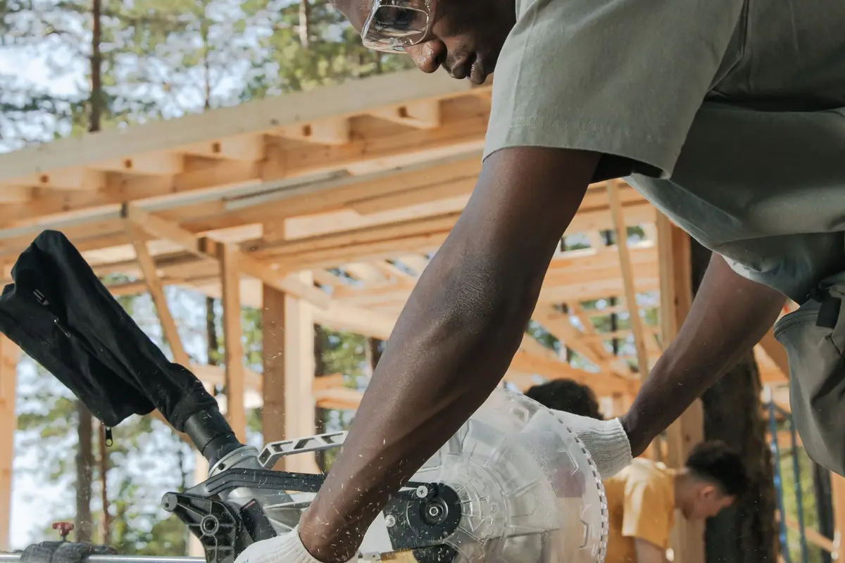 A carpenter in safety glasses cutting wood with a power saw
