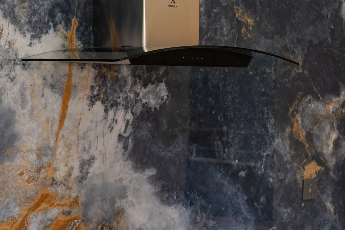 A glass and steel range hood against a dark marble backsplash