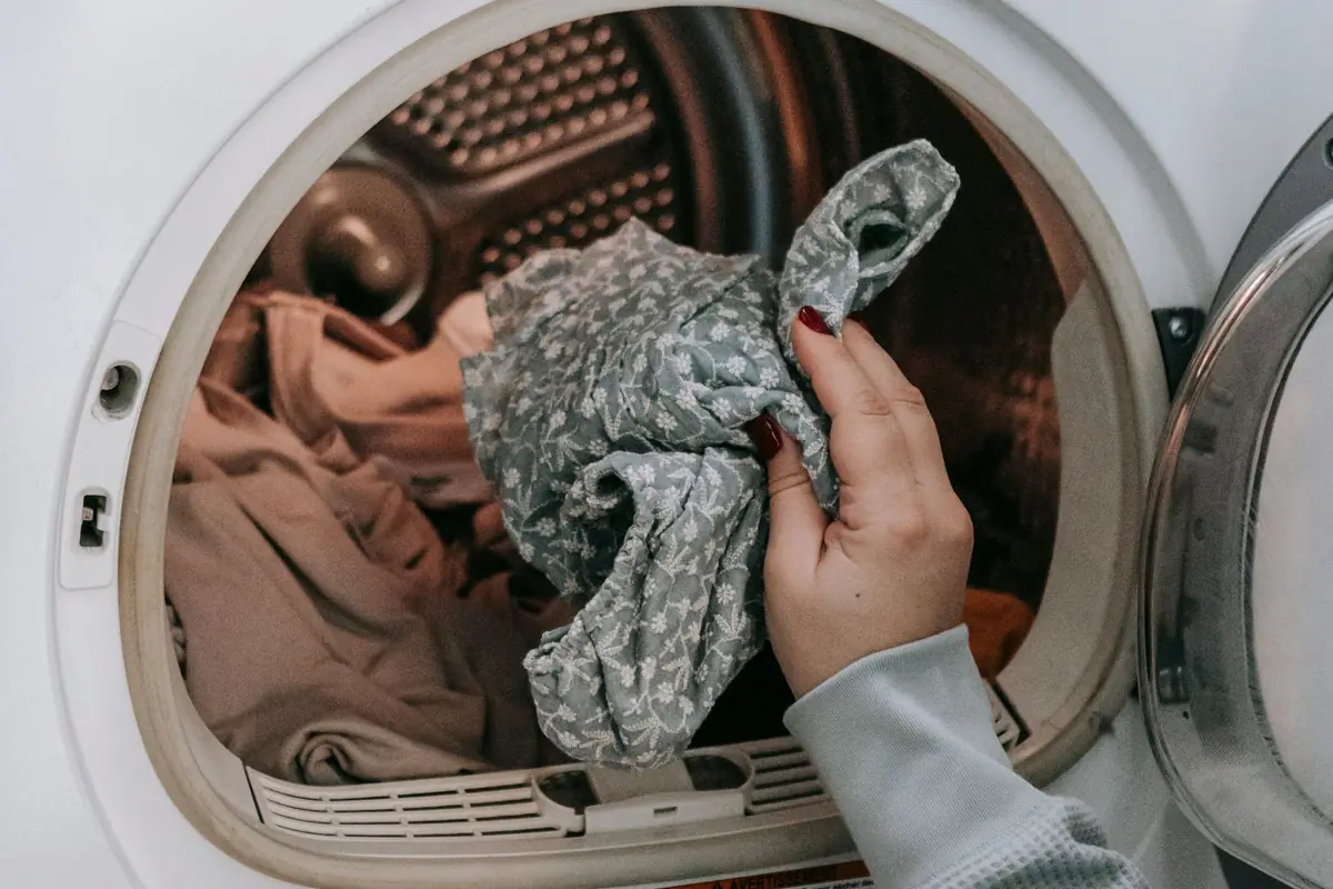 A hand loading clothes into a front-loading machine