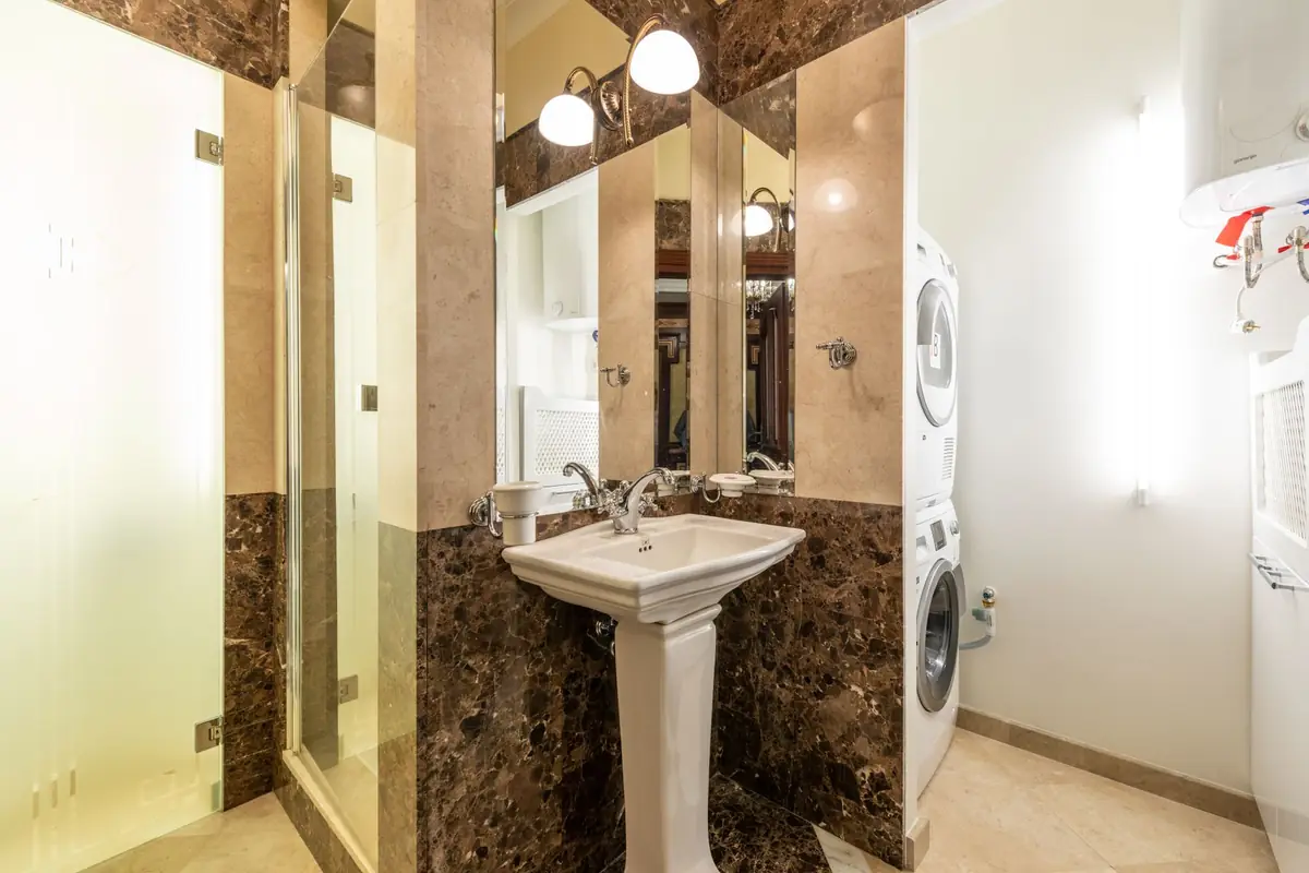 A marble bathroom with a stacked washer and dryer next to a pedestal sink