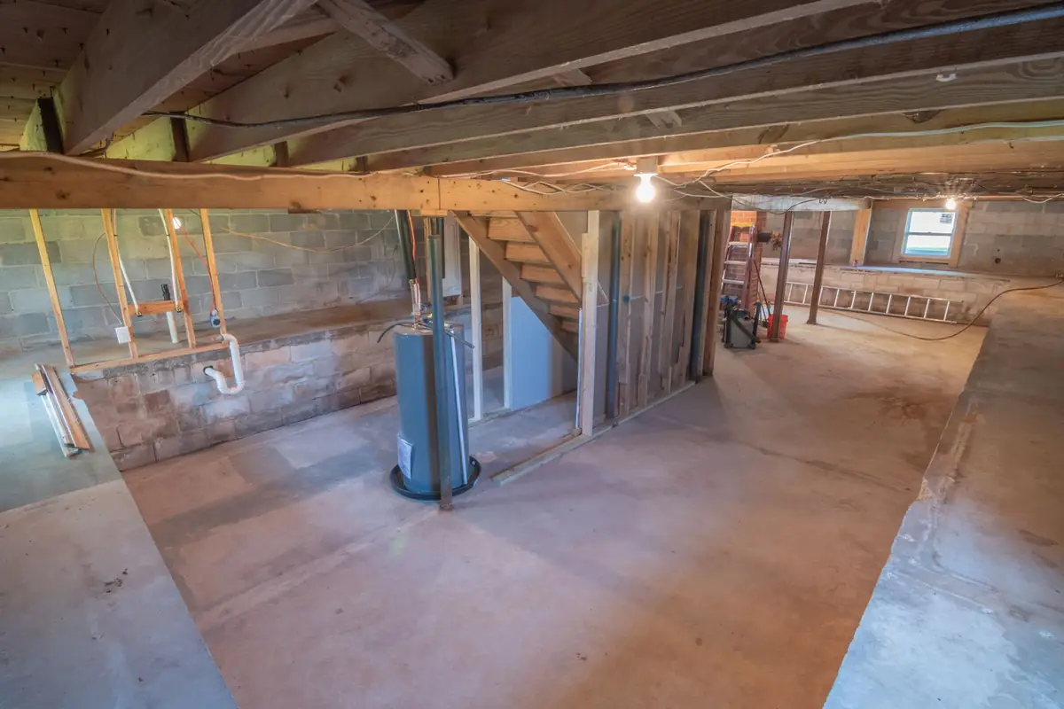 An unfinished basement with exposed beams, plumbing and a blue water tank