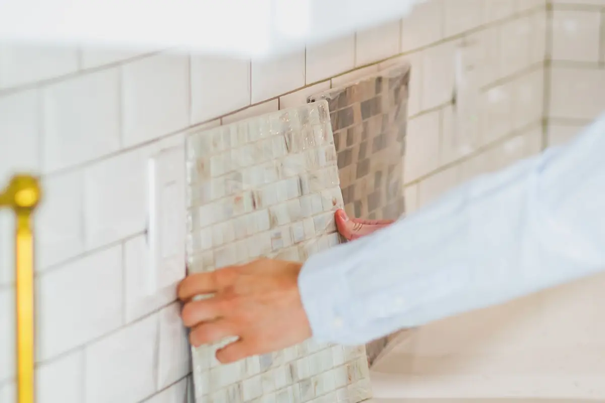 Hands pressing a tile into place on a kitchen backsplash