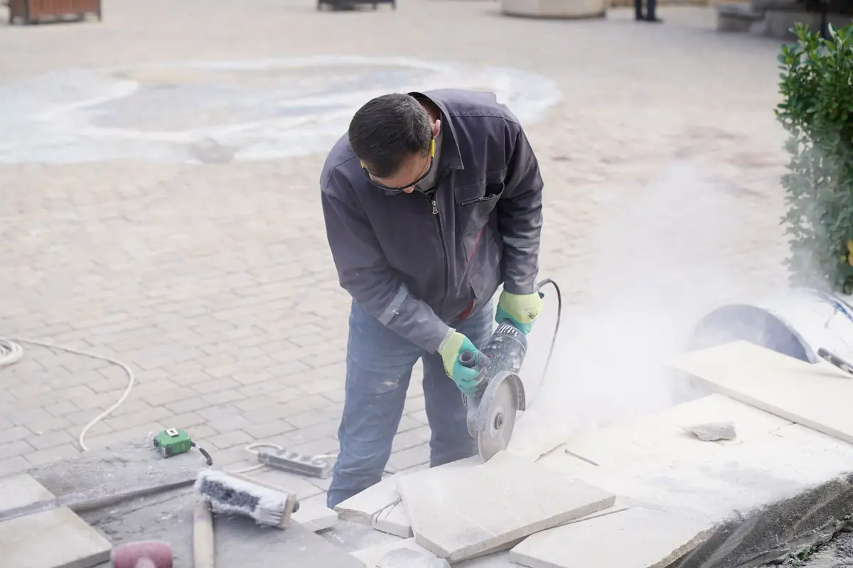 A worker cutting stone tiles with a power saw outdoors