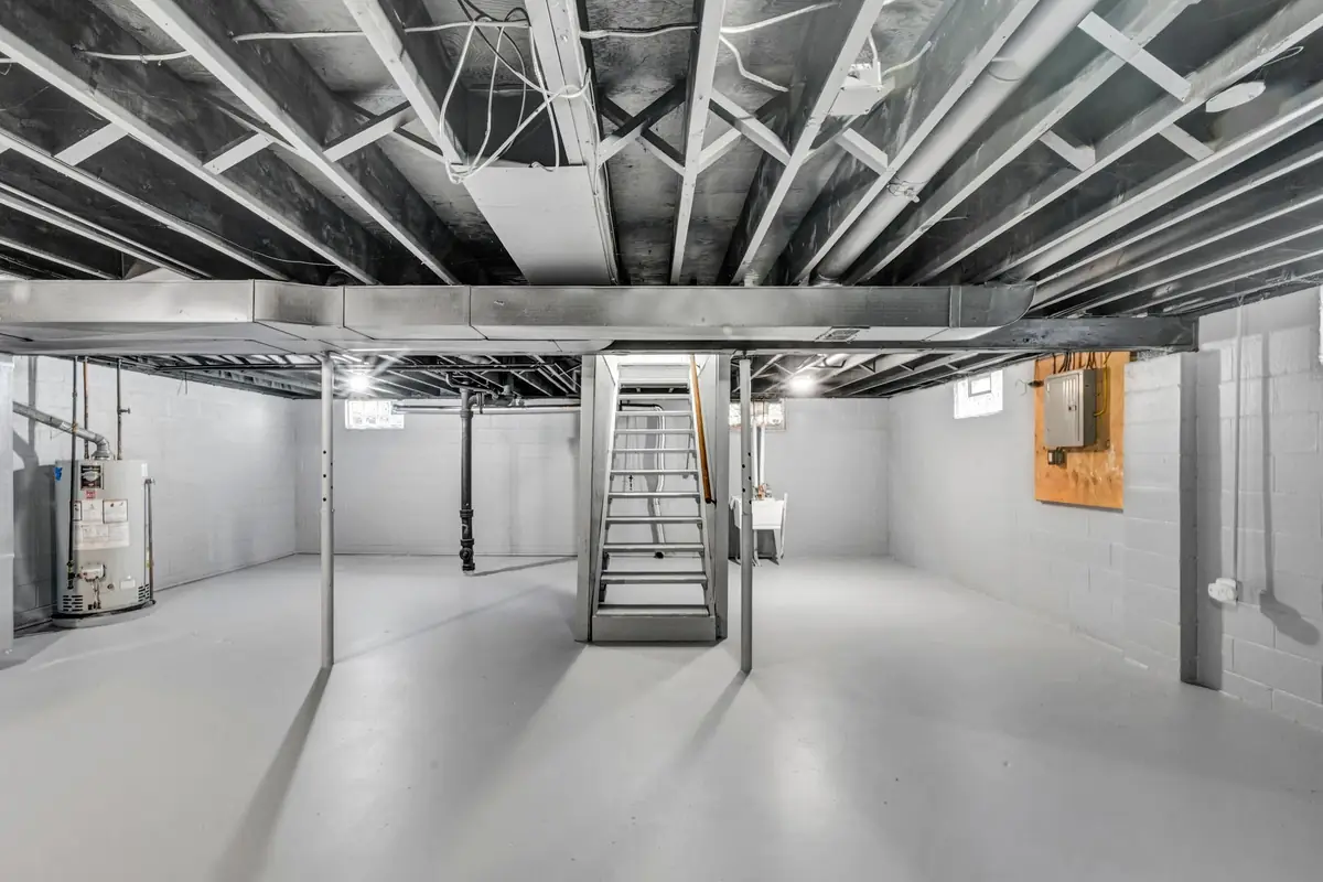 A clean unfinished basement with exposed ceiling joists and a staircase