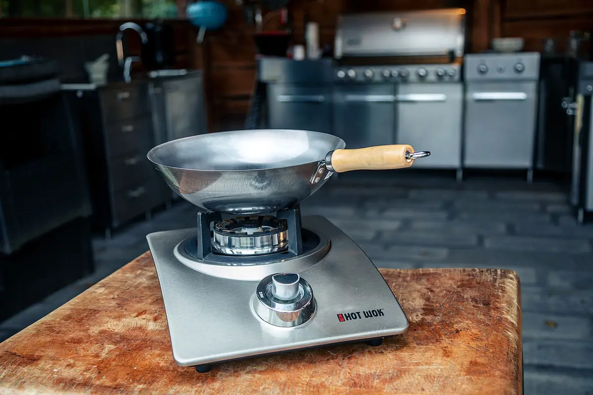 A steel wok sitting on a single burner on a wooden block