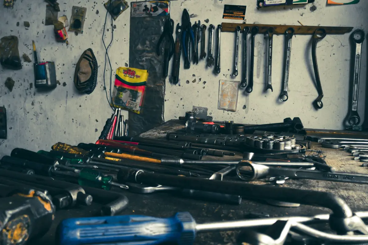 Hand tools spread across a garage workbench under a wall of wrenches