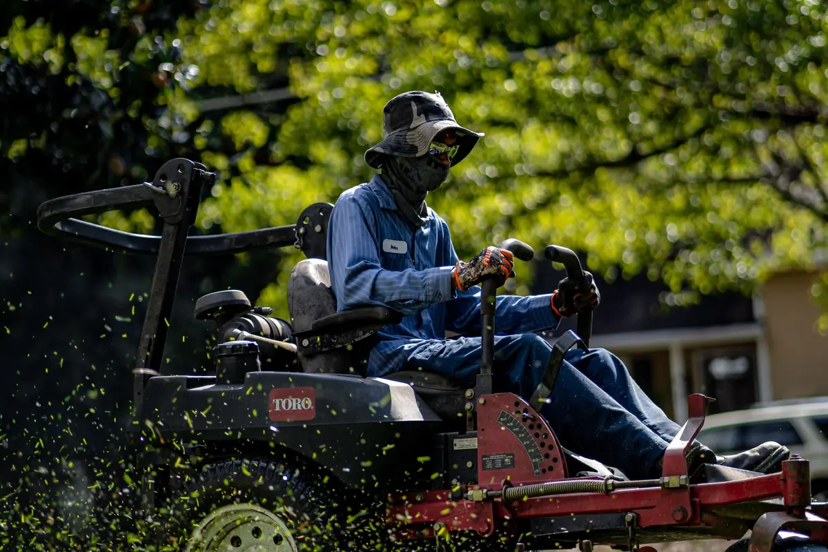 A person on a red riding mower cutting grass in a sunny park