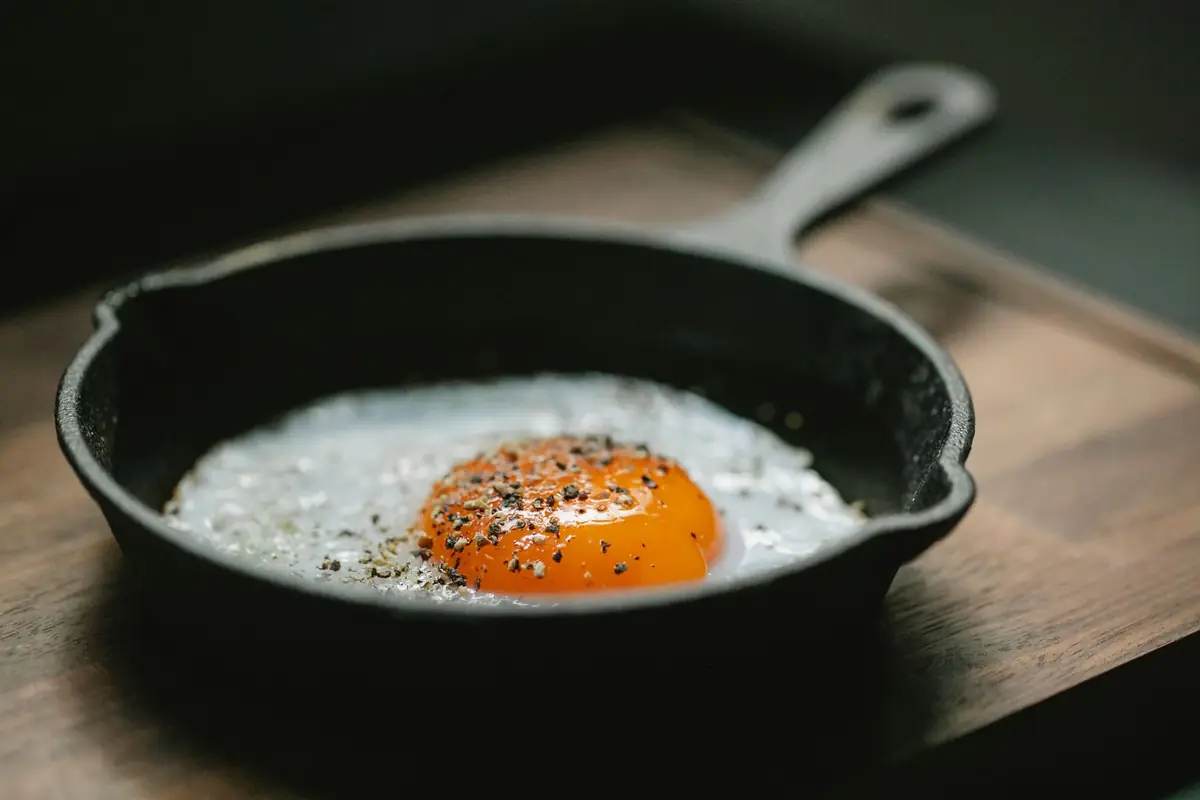 A fried egg in a small black cast iron skillet on a wooden board