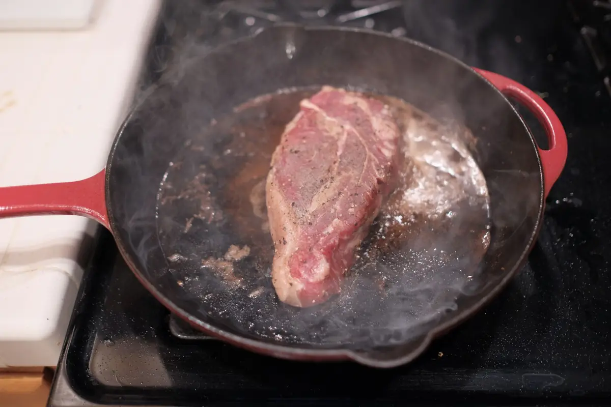 A steak searing in a hot cast iron pan on a stovetop