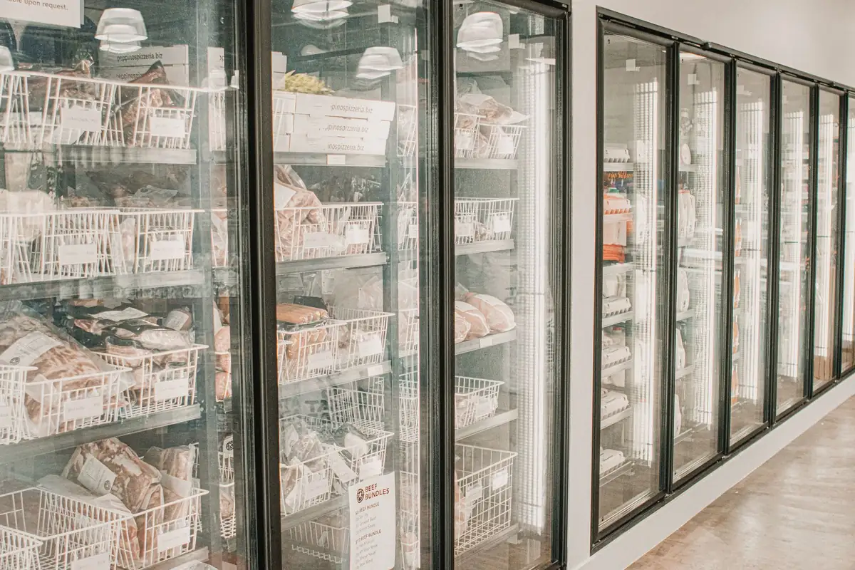 A row of upright freezers with glass doors and organized shelves