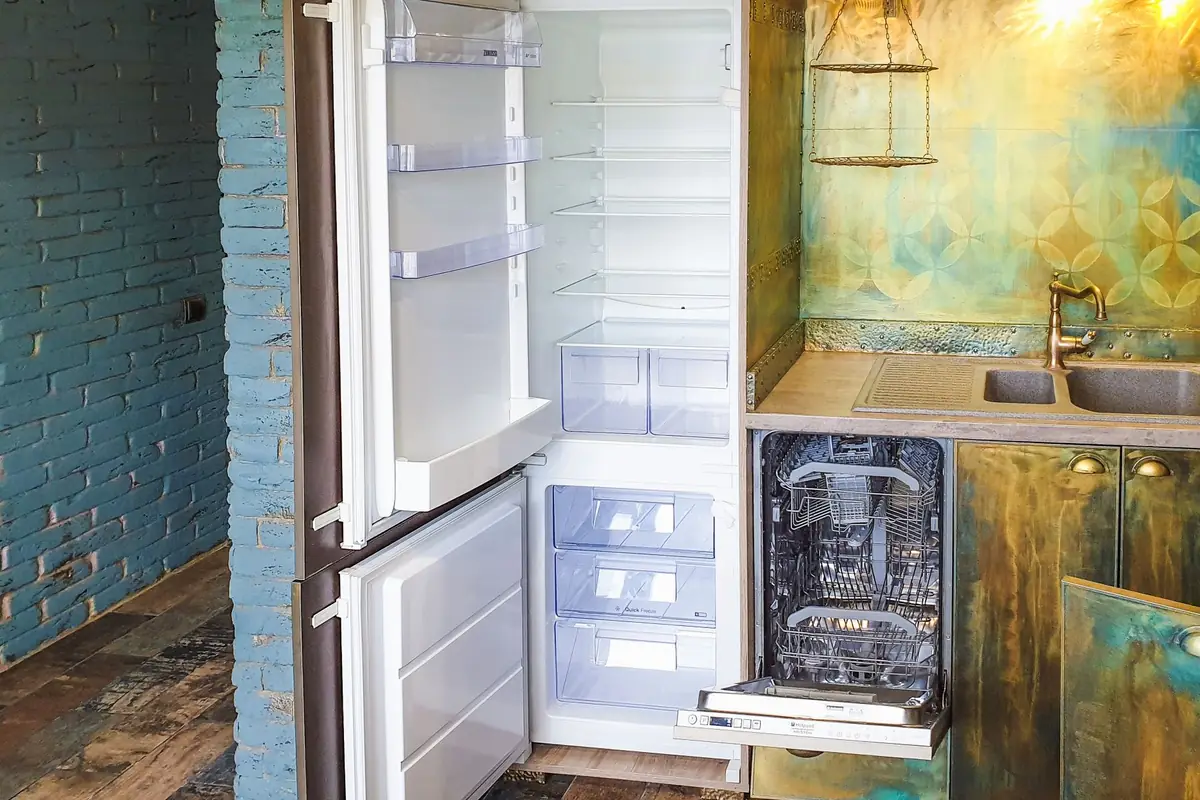 A narrow dishwasher fitted beside an open refrigerator in a small kitchen