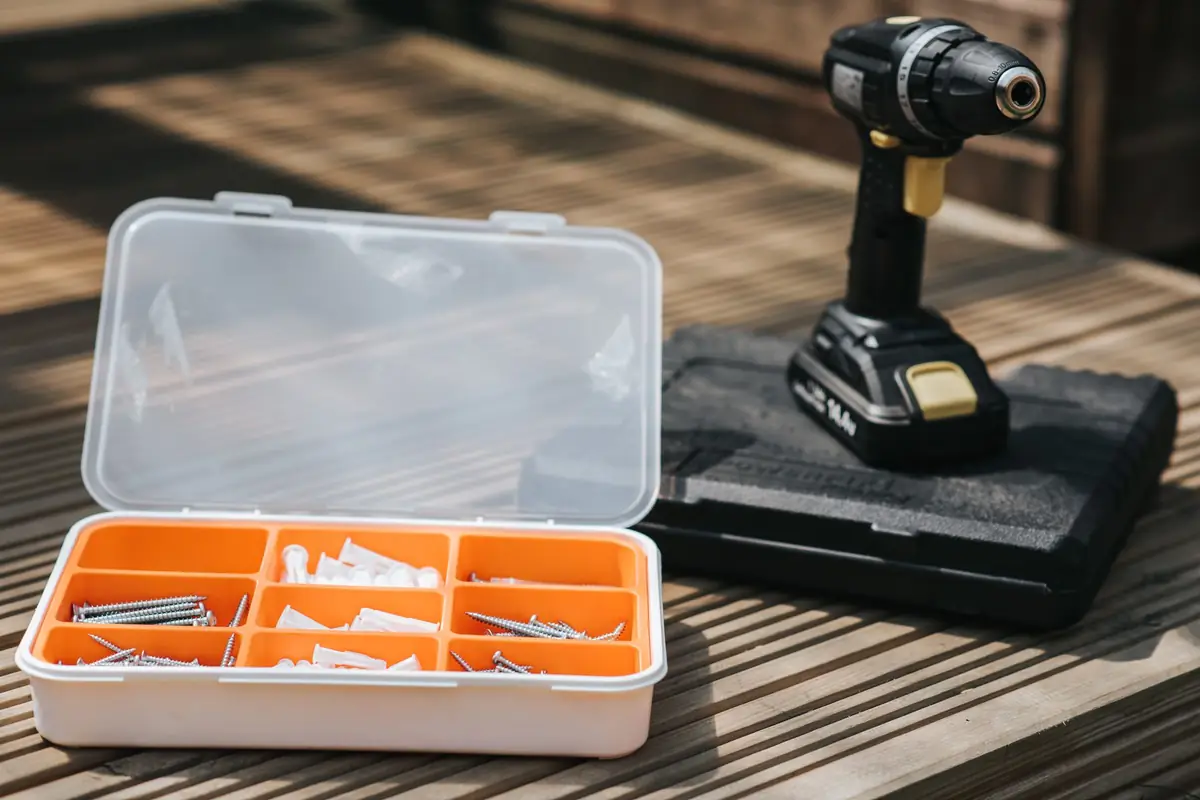 A compact cordless driver on its case next to an organizer box of screws