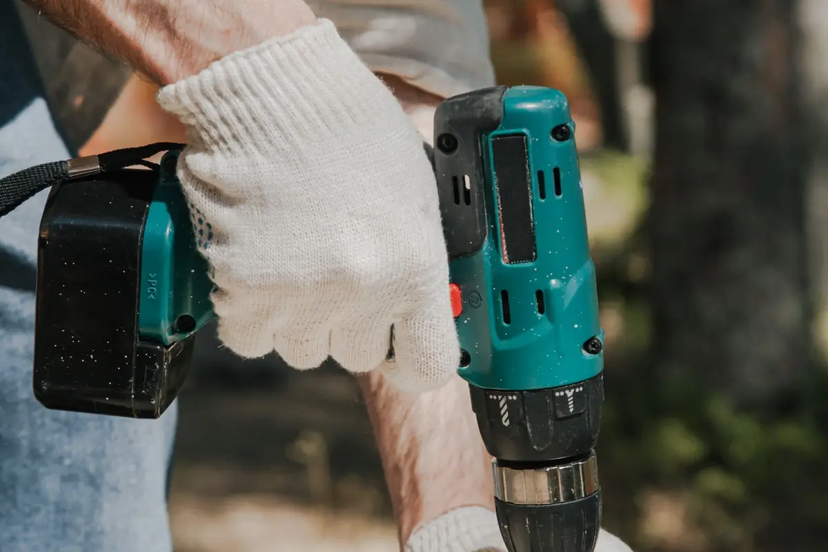 A worker in gloves driving into a wood panel with a cordless drill