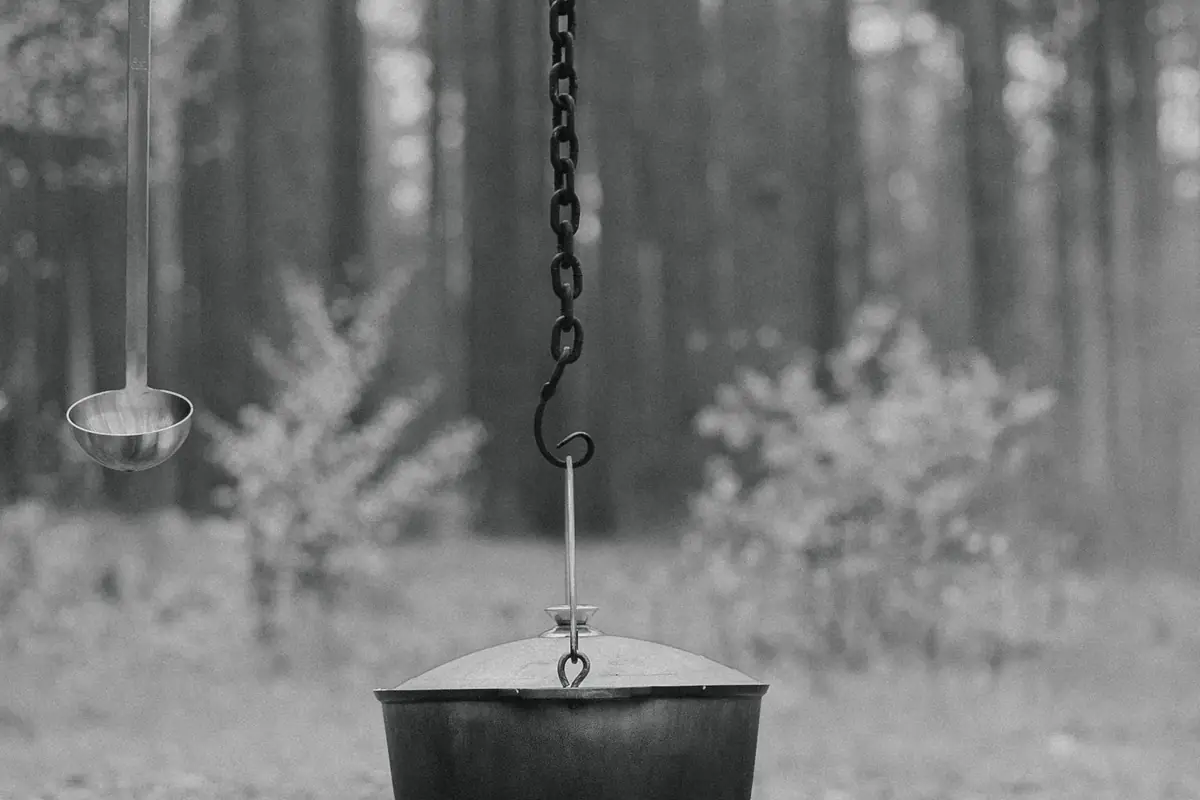 A black cast iron pot hanging over a campfire in the woods