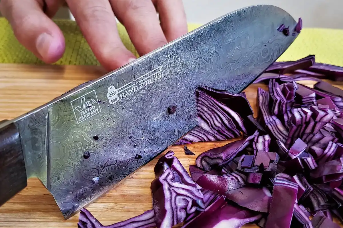 A patterned steel knife slicing red cabbage