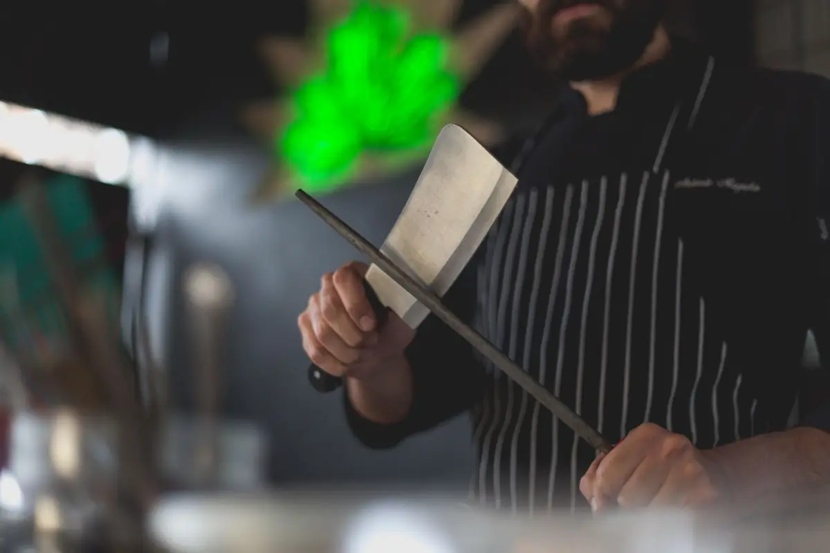 A chef in a striped apron honing a wide-bladed knife on a steel