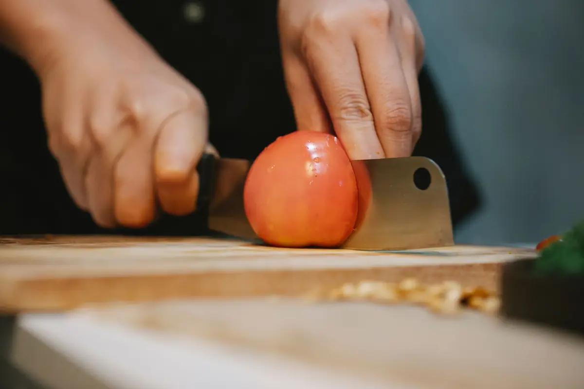 A knife slicing through a ripe tomato on a cutting board