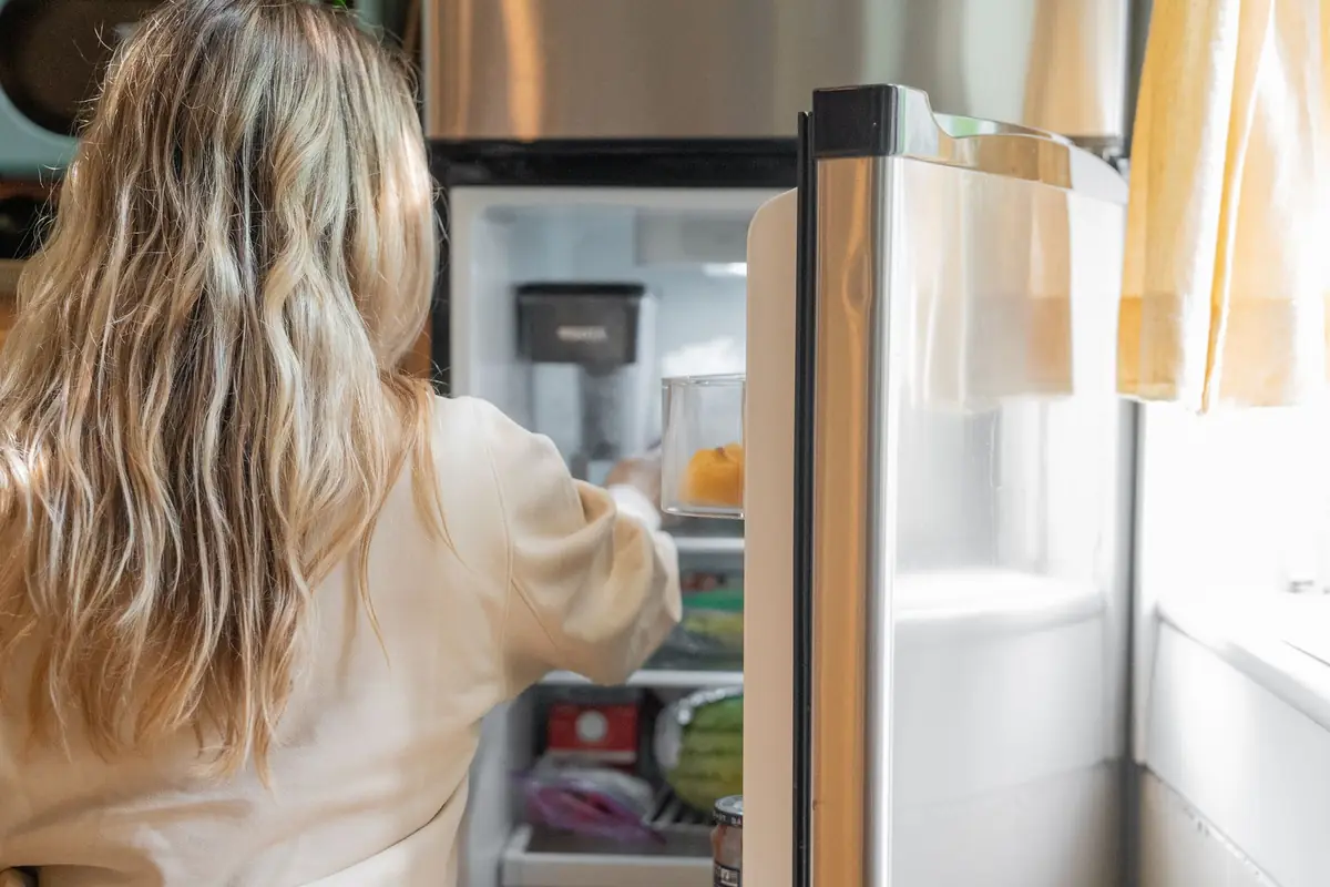 A woman reaching into an open refrigerator