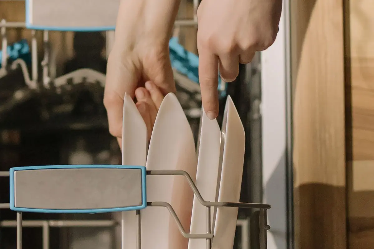 Hands loading plates into a dishwasher rack