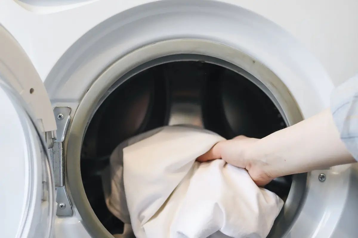 A hand putting laundry into a front-load washer