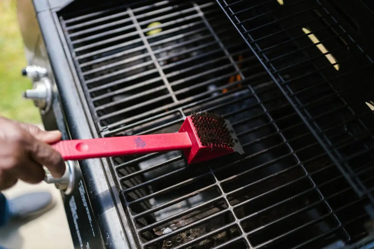 Scrubbing a grill grate with a red grill brush