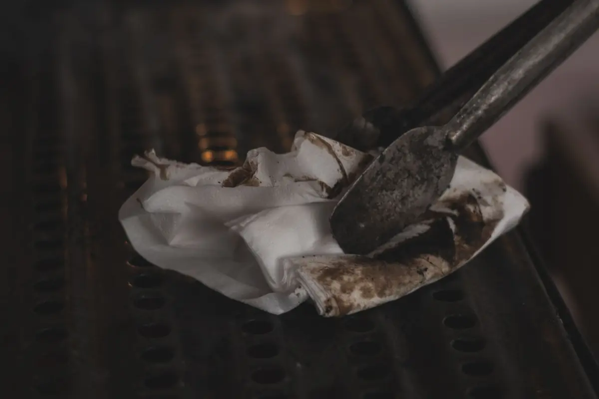 Tongs and a cloth wiping a dirty grill grate