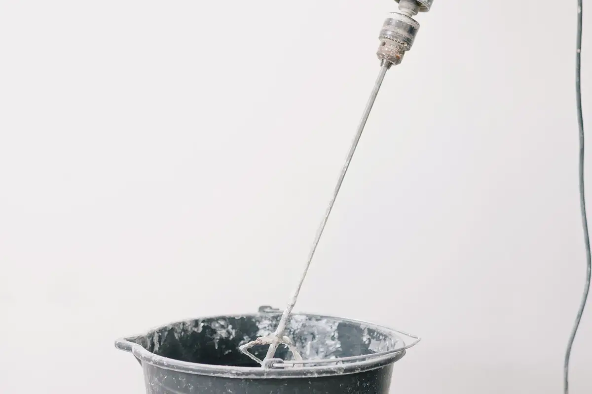 A drill fitted with a mixing paddle stirring a bucket of mortar
