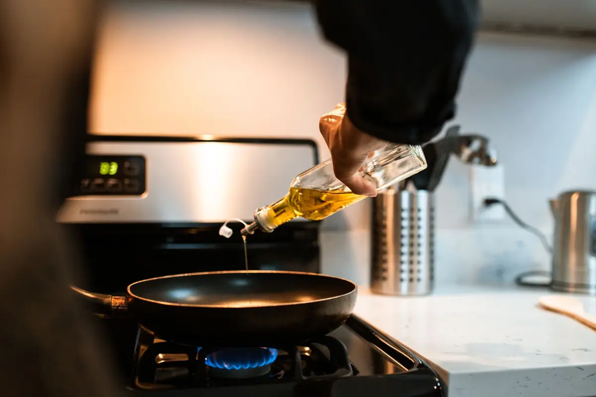 Oil being poured into a skillet on a gas stove