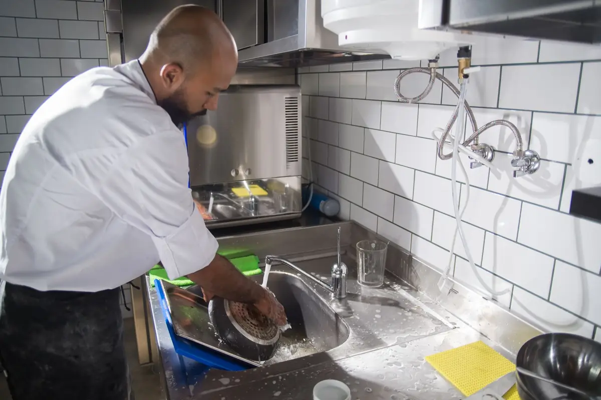 A cook scrubbing a pan under the faucet in a kitchen sink