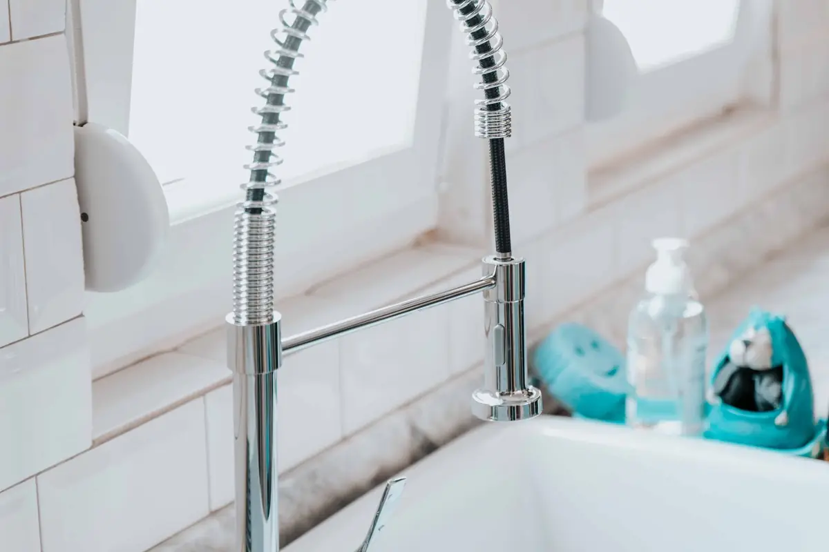 A chrome pull-down kitchen faucet over a white sink by a window