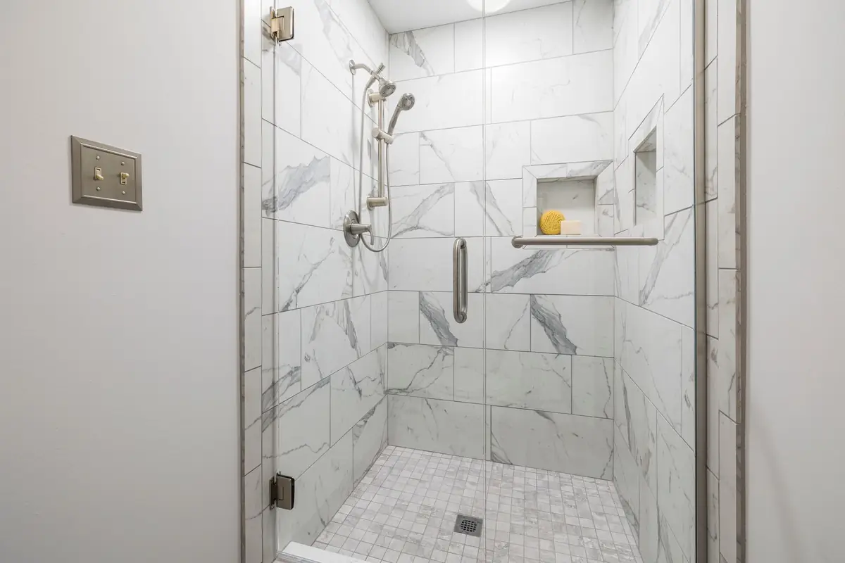 A shower with white marble tile and clean grout lines
