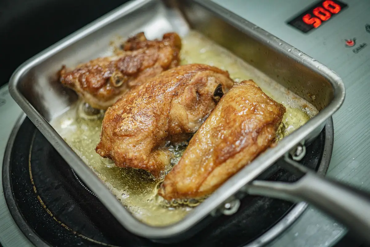 Chicken thighs browning in a rectangular steel pan