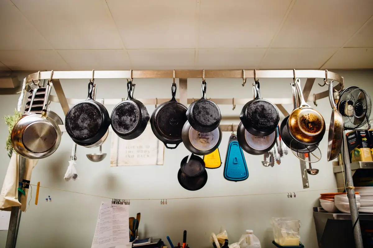 Dark seasoned pans and pots hanging on a rail in a home kitchen