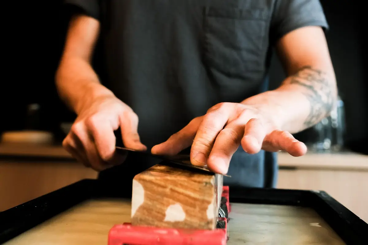 Hands pushing a knife across a whetstone held in a red non-slip base