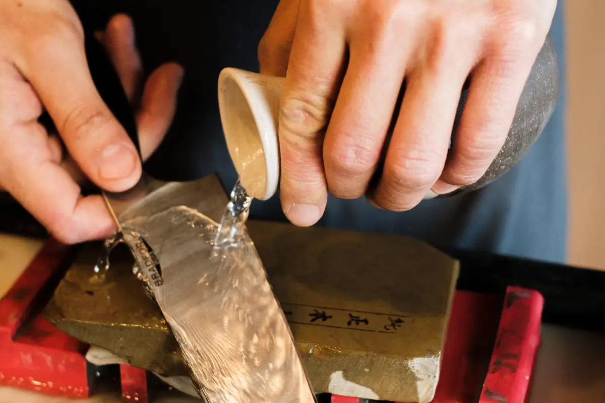 Water being poured over a whetstone before sharpening a knife