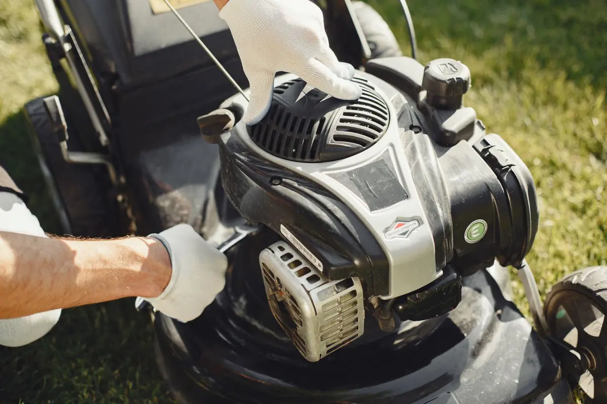 Gloved hands working on a push mower engine