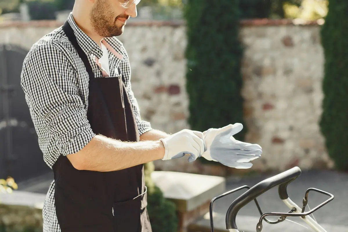 A man in an apron pulling on work gloves before yard work