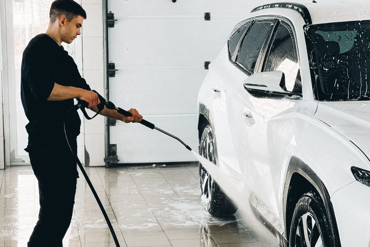 A man using a pressure washer on a white car inside a garage