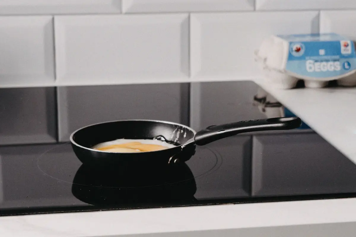 An egg cooking in a flat-bottomed frying pan on a glass cooktop
