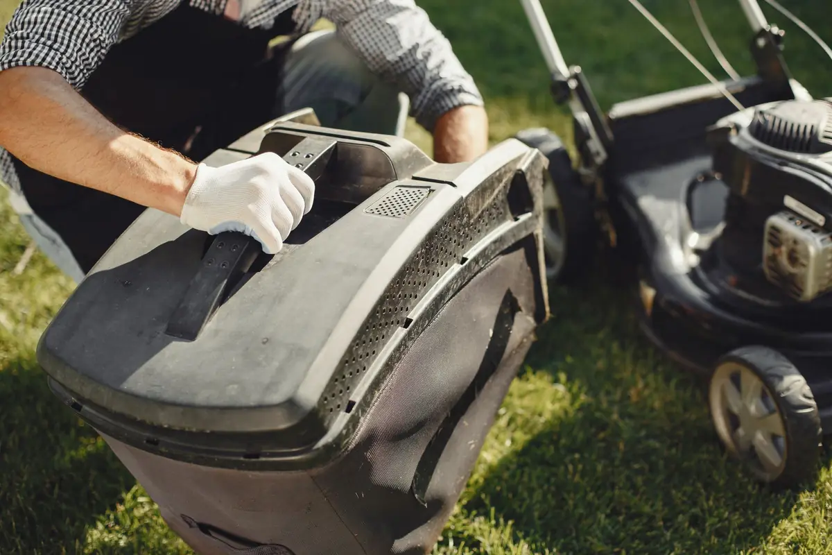 Gloved hands lifting the grass bag off a push mower