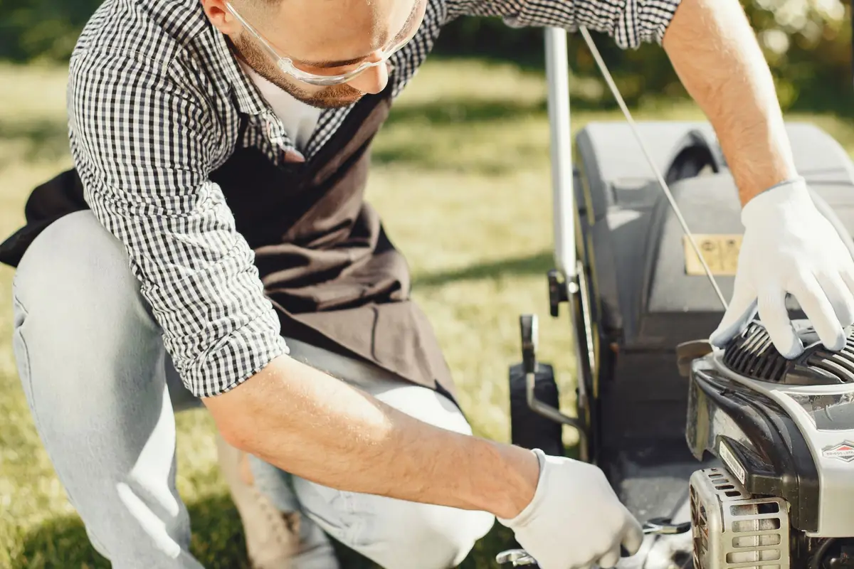 A man in work gloves checking a push mower in a garden