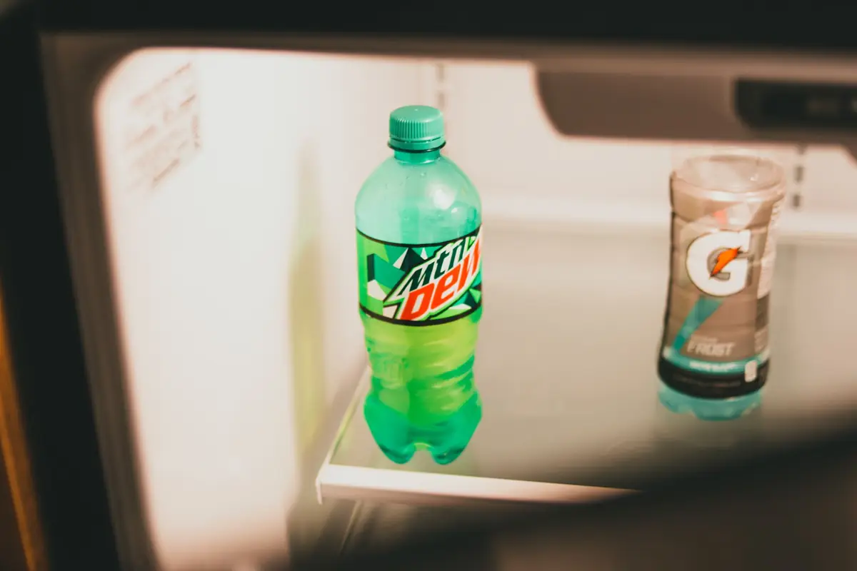 Two bottles of soda on a shelf inside an open fridge